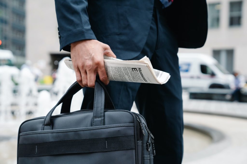 Hand eines Geschäftsmanns, der eine Zeitung und Aktentasche trägt